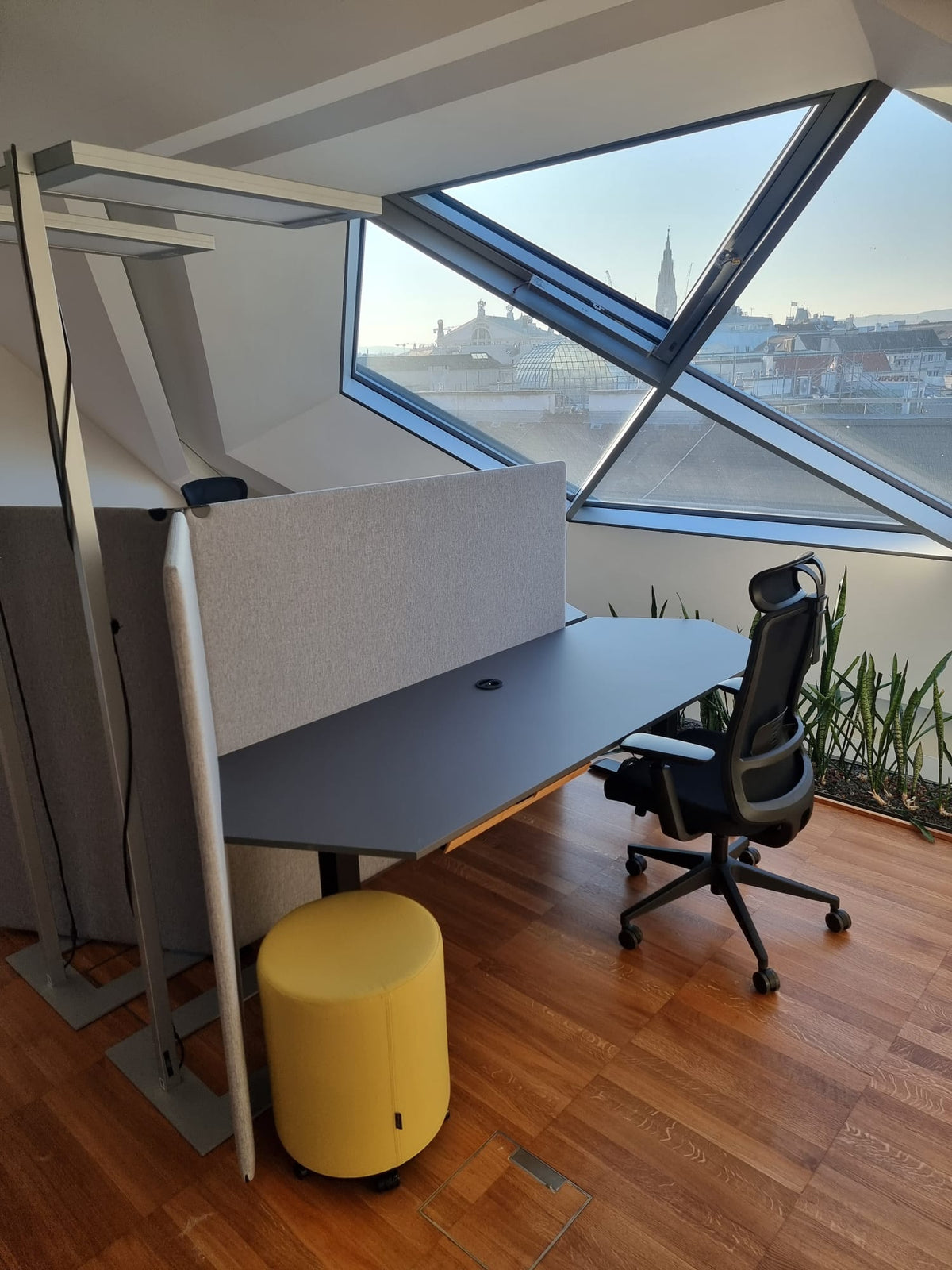 Arbeitsplatz im Dachgeschoß mit höhenverstellbarem Schreibtisch, Akustik-Trennwand und Blick über die Wiener Dächer