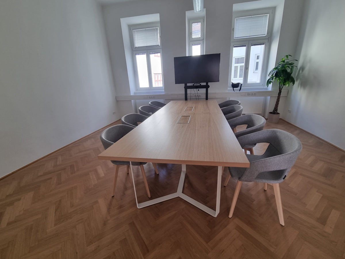 Besprechungsraum im Wiener Altbau mit Eichentisch auf weißem Kufengestell und grauen Schalenstühlen